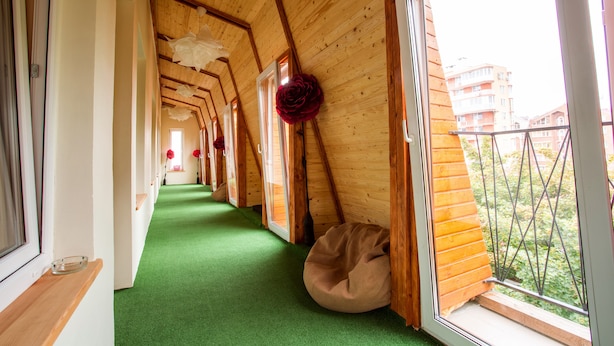 A corridor with wooden walls and green carpet, leading to a balcony with a view of buildings. - Hostel Tarnopil (Ternopil)