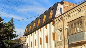 A multi-story building with a row of windows on the ground floor, a visible storefront with signage, and a parked car in front. - Hostel Tarnopil (Ternopil)