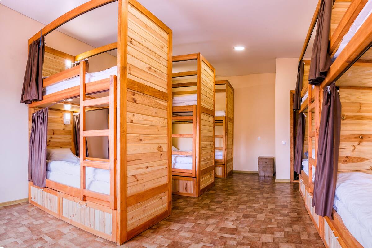 A room with bunk beds made of wood, a tiled floor, and a small trash bin.