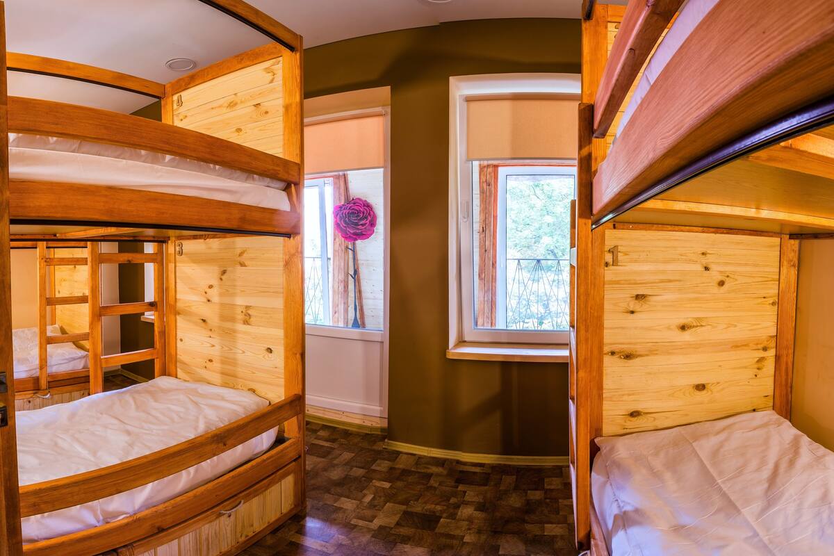 A room with bunk beds, a window with a view, and a wooden floor.