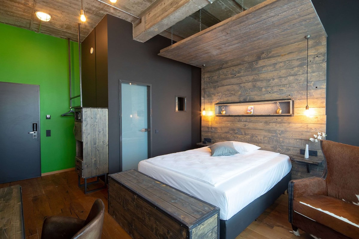 A modern bedroom with a large bed, a bench, a wooden wall, and a green wall.