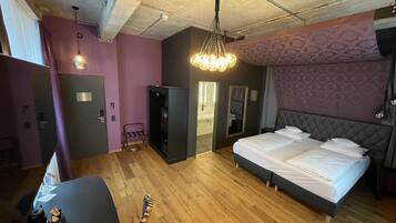 Una habitación de hotel moderna con una cama grande, un armario, un escritorio con una guitarra y una lámpara colgante.