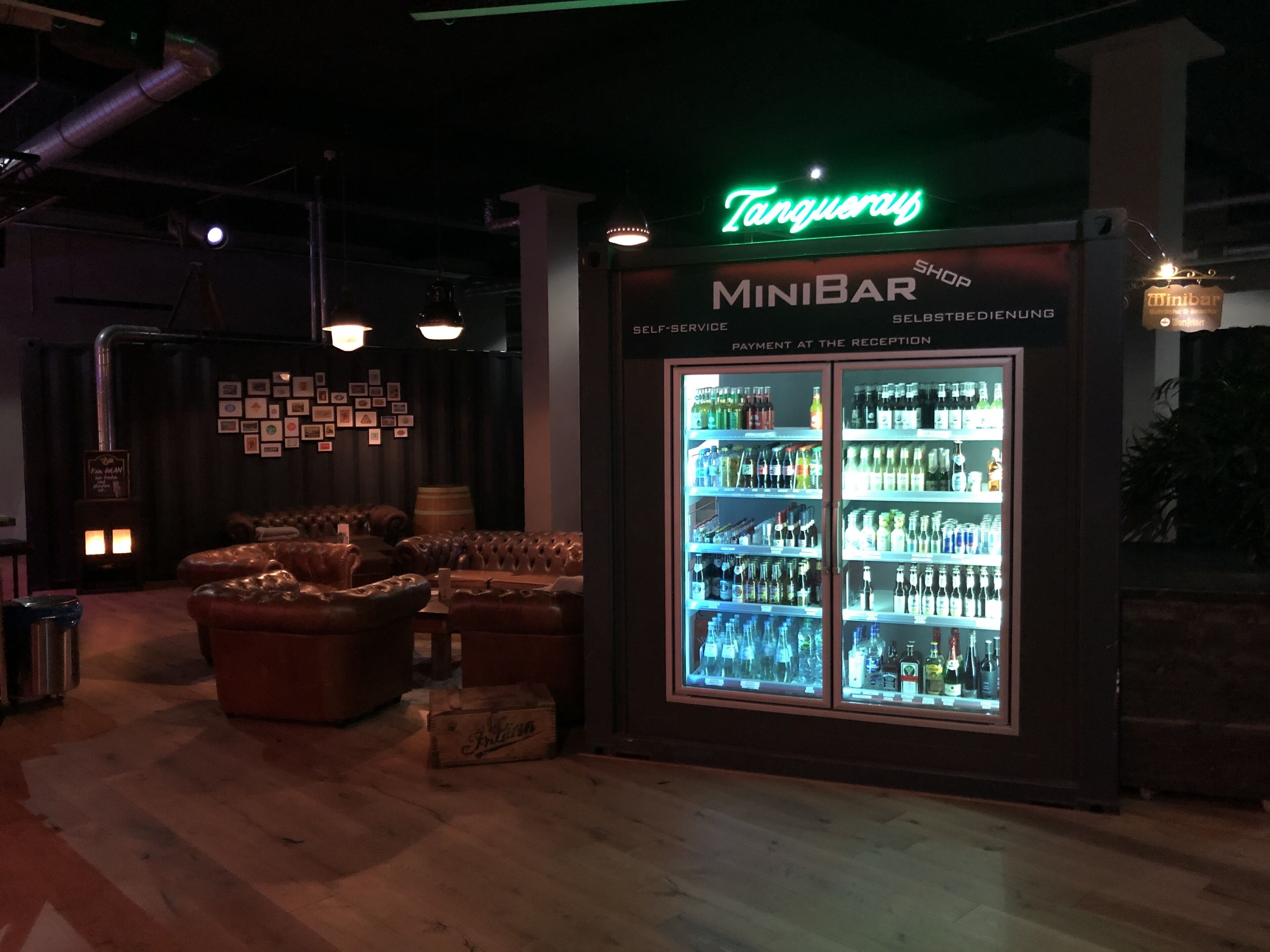 Een minibar met een neonbord, een koelkast vol drankjes, leren zitplaatsen en een houten vloer.