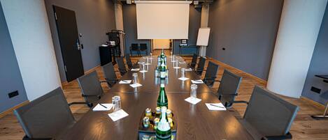 Un salón de conferencias con una larga mesa, sillas, una pantalla de proyector y una pizarra.