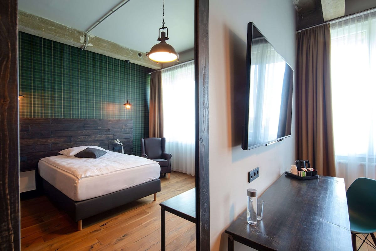 A hotel room with a bed, a desk, a chair, a TV, and a window with curtains.