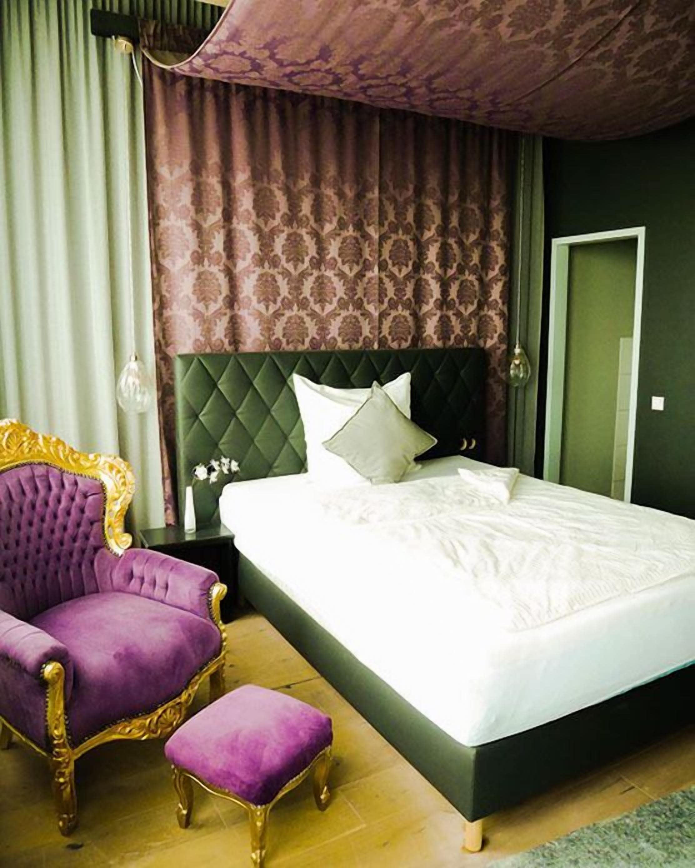 A bedroom with a large bed, a purple armchair, and a matching ottoman.