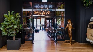 A restaurant entrance with a sign reading "HAVN RESTAURANT," a mannequin, and a potted plant. - LOFTSTYLE Hotel Hannover, Best Western Signature Collection (Hannover)