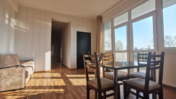 Uma sala de estar ampla com piso de madeira, uma mesa de jantar com cadeiras, um sofá e uma grande janela que oferece vista para o exterior.