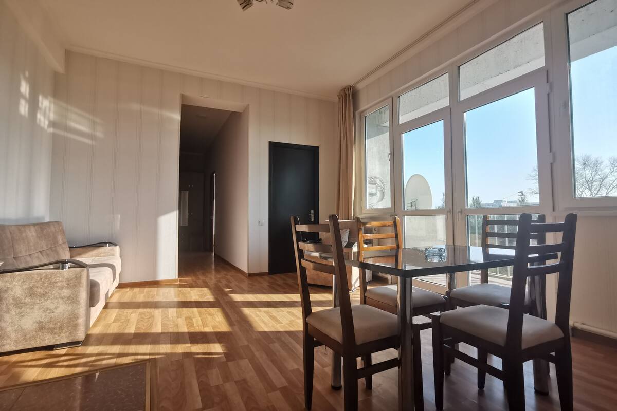 Un vaste espace de vie doté d’un plancher en bois, d’une table à manger avec des chaises, d’un canapé et d’une grande fenêtre offrant une vue sur l’extérieur.
