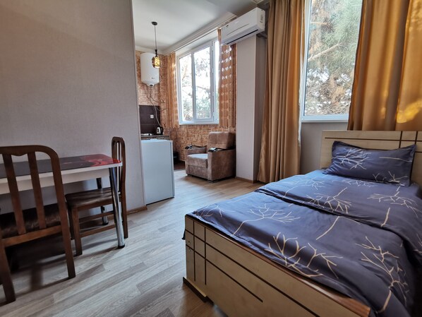 A bedroom with a bed, a desk, and a kitchenette.