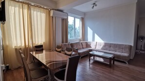 Uma sala de estar com uma mesa de jantar de vidro, dois sofás e uma televisão fixada na parede.