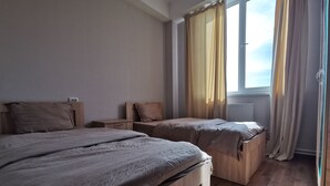 Quarto com duas camas, janela com cortinas e radiador.