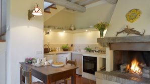 A cozy kitchen with a fireplace, wooden beams, and a dining area with a table and chairs. - Casa di Lilli (Castiglione d'Orcia)