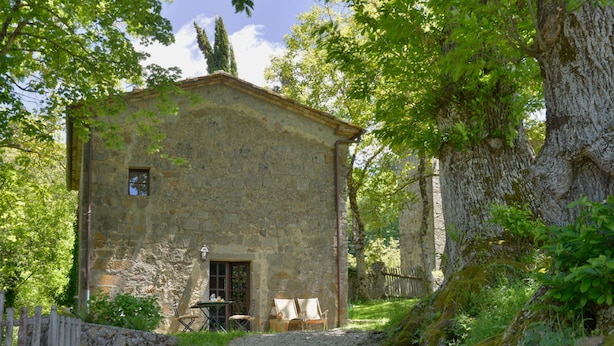 A rustic stone building with a door and windows, surrounded by greenery and a wooden fence. - Casa di Lilli (Castiglione d'Orcia)