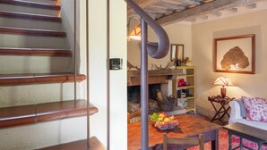 A wooden staircase leading to a living area with a fireplace, a dining table with fruit, and a sofa with patterned cushions. - Casa di Lilli (Castiglione d'Orcia)
