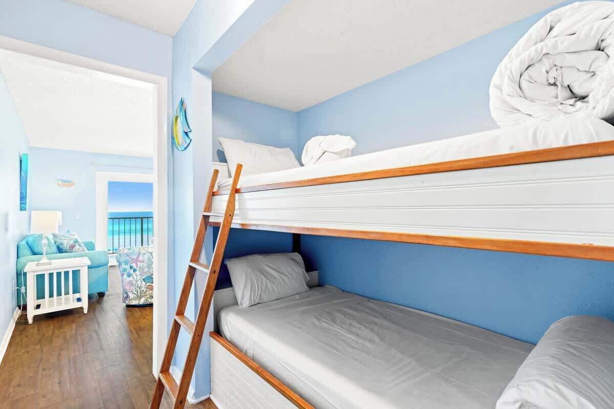 Een slaapkamer met stapelbed, een houten trapje, een klein wit tafeltje en een blauwe muur.