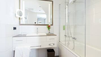 A modern bathroom with a large mirror, white cabinetry, a glass shower enclosure, and a small plant on the vanity.