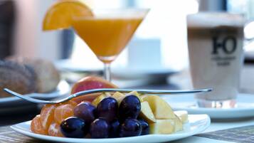 Un desayuno con un plato de fruta, un vaso de jugo de naranja y una taza de café.
