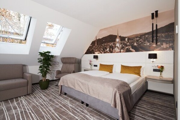 A modern bedroom with a bed, a sofa, a potted plant, and a cityscape mural on the wall.