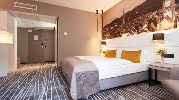 A hotel room with a large bed, a nightstand, a wall-mounted lamp, and a cityscape mural.