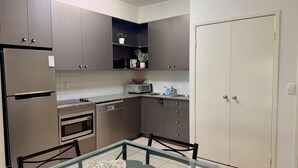 Een praktische keuken met een koelkast, magnetron, oven en een kleine eethoek met stoelen en een glazen tafel.