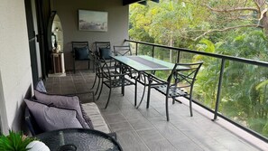 A balcony with a table and chairs, a sofa, and a view of greenery.