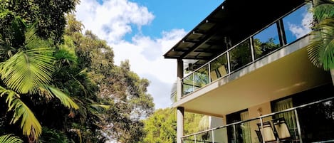 Un edificio moderno su due piani, con ampie finestre e un balcone, immerso nel verde.