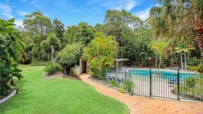 A well-maintained garden with a swimming pool, surrounded by lush greenery and trees. - Baden 45 - Rainbow Shores. Beachside Unit for the family. Aircon. Swimming Pool. Tennis Court (Rainbow Beach)