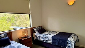 Een slaapkamer met twee enkele bedden, een nachtkastje met lamp, een raam met uitzicht op groen en een wandlamp.