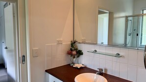 A bathroom with a white sink, a glass shelf, a mirror, and a door.
