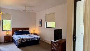 A bedroom with a bed, bedside lamps, a ceiling fan, a television, and windows with blinds.