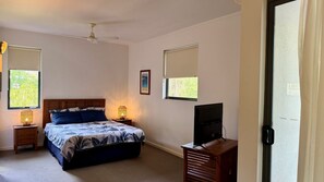 A bedroom with a bed, bedside lamps, a ceiling fan, a television, and windows with blinds.