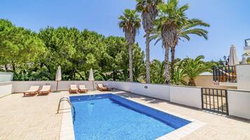 Een buitenzwembad, ligstoelen bij het zwembad