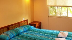 Un dormitorio con cama, mesita de noche y ventana con vista a palmeras.
