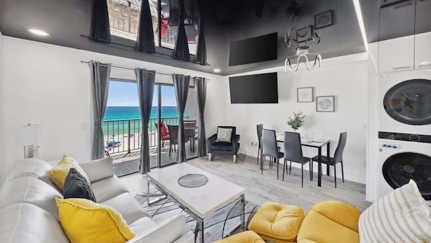 A modern living room with a sofa, yellow cushions, a dining area, and a view of the ocean.