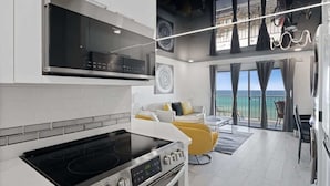 A modern kitchen with a stove, oven, and microwave. There is a dining area with yellow chairs and a view of the ocean.
