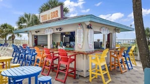 Un bar tiki con sillas y mesas coloridas, un cartel de menú y un cielo despejado.