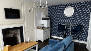 A modern living room with a fireplace, a blue sofa, a wooden coffee table, a TV mounted on the wall, and a patterned wallpaper. - The Little Angel (Whitby)