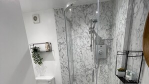 A modern bathroom with a glass-enclosed shower, a white toilet, and a white sink. - The Little Angel (Whitby)