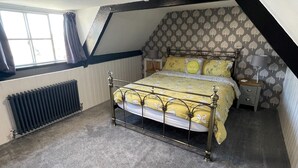 A bedroom with a sloped ceiling, a radiator, a bed with a metal frame, and patterned wallpaper. - The Little Angel (Whitby)