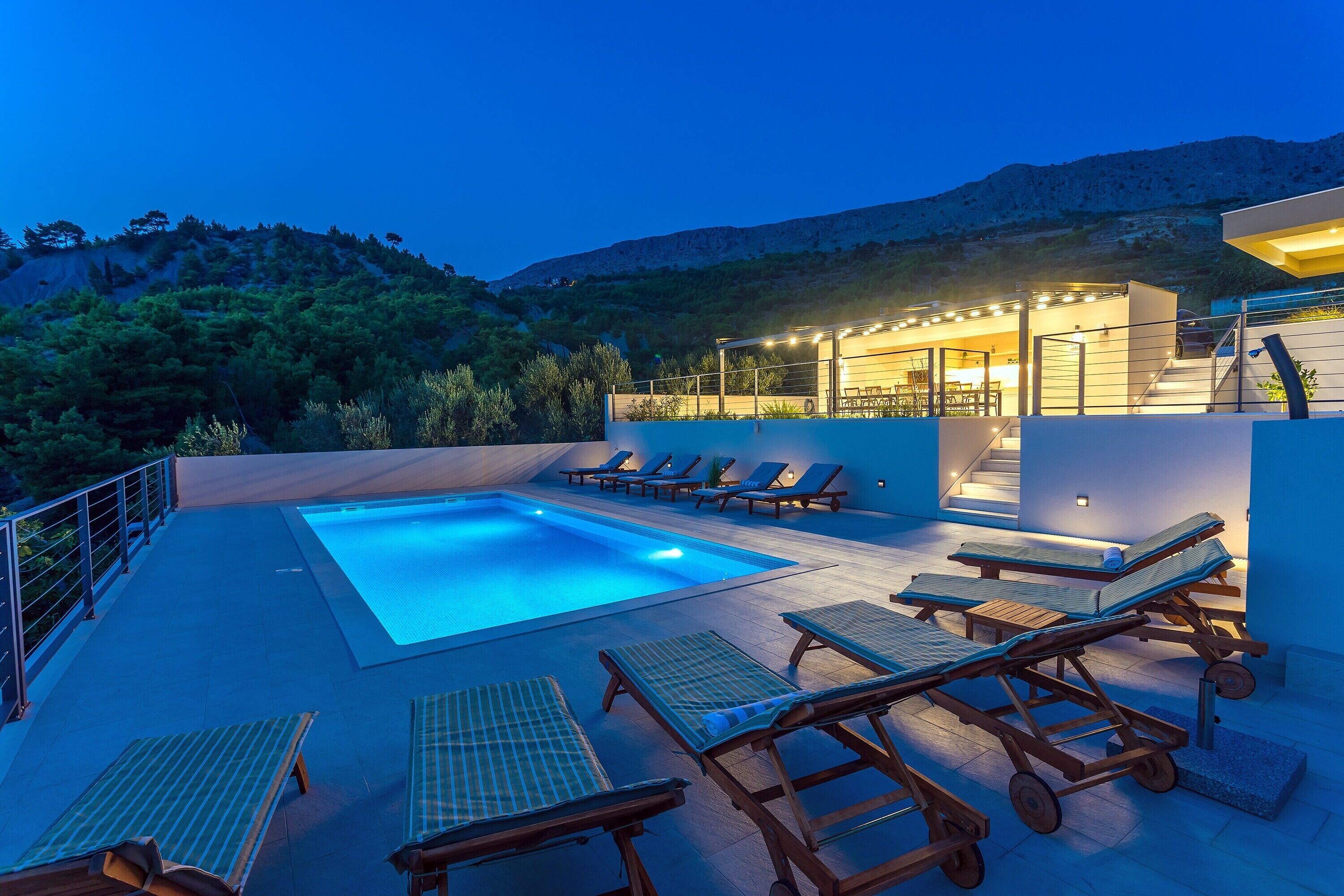 A rooftop pool area with lounge chairs and a swimming pool, surrounded by a mountainous landscape.
