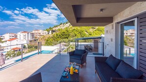 A balcony with wicker furniture, a table with drinks, and a view of a swimming pool and buildings. - Villa Diva with 7 bedrooms, heated pool, sauna and fun zone, sea views (Podstrana)