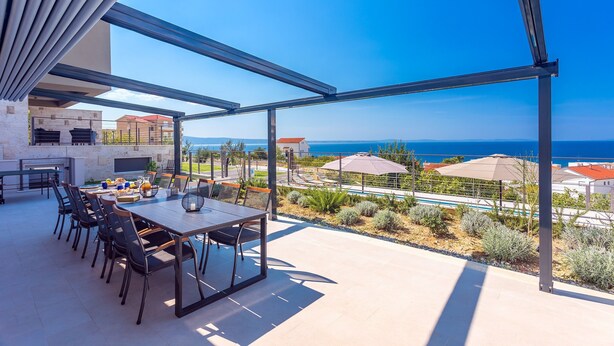 An outdoor patio with a dining table and chairs, overlooking a pool and the sea. - Villa Diva with 7 bedrooms, heated pool, sauna and fun zone, sea views (Podstrana)