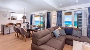 A modern living room with a brown sofa, a dining table with chairs, and a kitchen area in the background. - Villa Diva with 7 bedrooms, heated pool, sauna and fun zone, sea views (Podstrana)