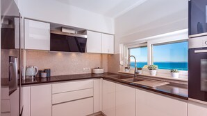 A modern kitchen with white cabinets, a stainless steel refrigerator, and a window with a view of the sea. - Villa Diva with 7 bedrooms, heated pool, sauna and fun zone, sea views (Podstrana)