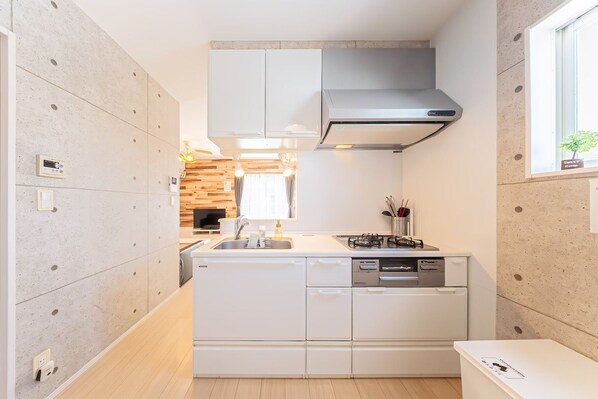 Cocina compacta con muebles blancos, estufa integrada y ventana con vistas.
