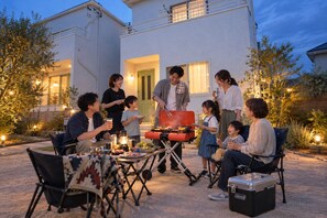 Un grupo de personas reunidas alrededor de una parrilla al aire libre, con una casa al fondo.