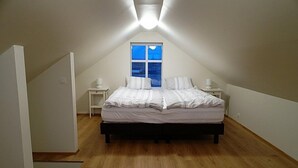 A bedroom with a sloped ceiling, a bed with white bedding, two bedside tables, and a window with a view of the sky.