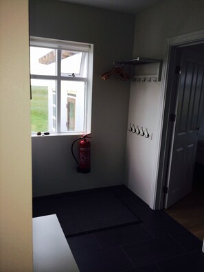Una habitación pequeña con ventana, extintor, puerta y un sistema de ganchos en la pared.