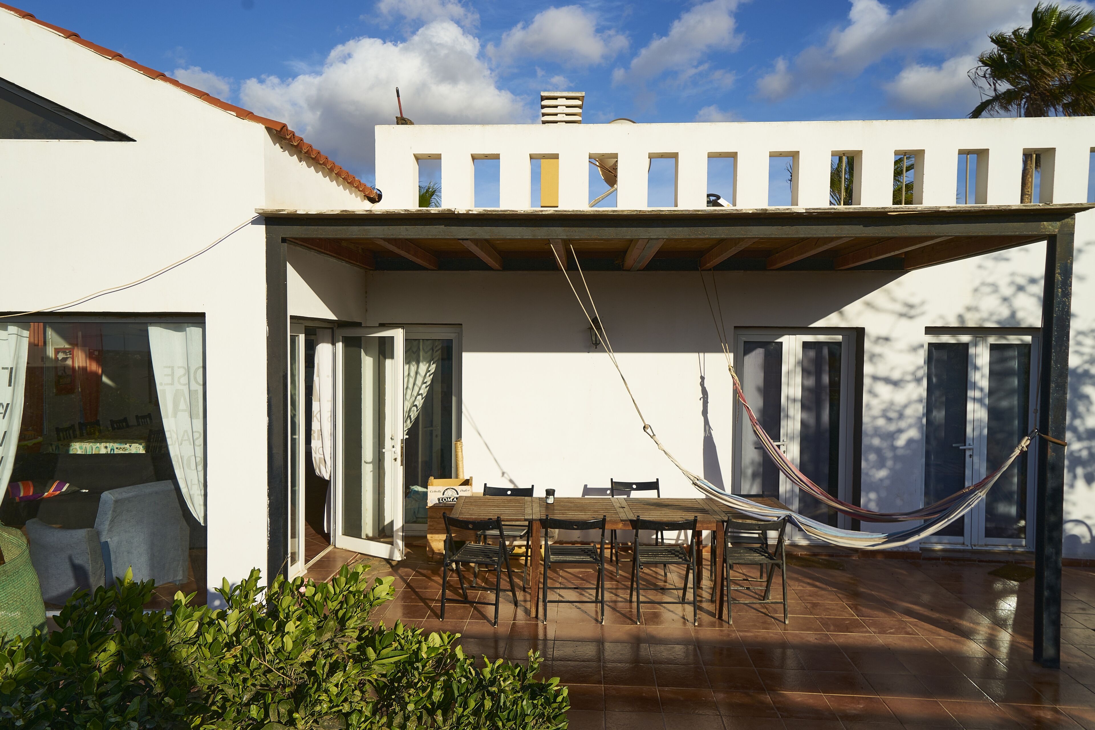 A patio with a table and chairs, a hammock, and a view of a white building with multiple windows.